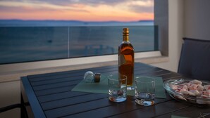 A table with a bottle, two glasses, and a bowl of snacks on a balcony with a view of the ocean at sunset. - Villa Four Brothers Middle Floor (Podstrana)