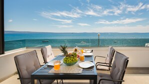 A table set with a fruit bowl, plates, and drinks on a balcony overlooking the sea. - Villa Four Brothers Middle Floor (Podstrana)
