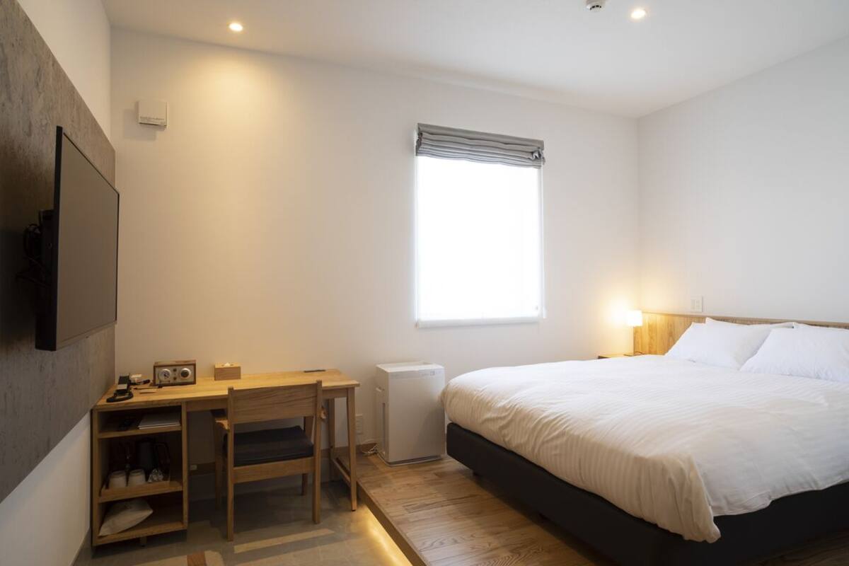 A bedroom with a bed, a desk, a chair, a radiator, and a window.