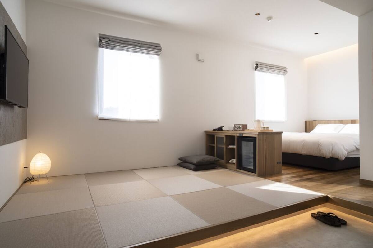A modern hotel room with tatami flooring, a bed, a desk with a lamp, and a TV.