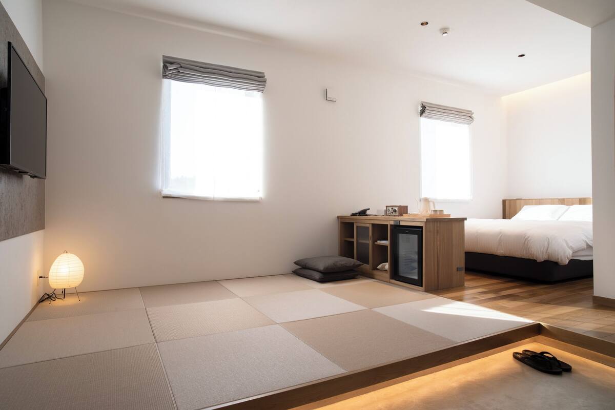 A modern bedroom with tatami flooring, a bed, a desk, and a TV.