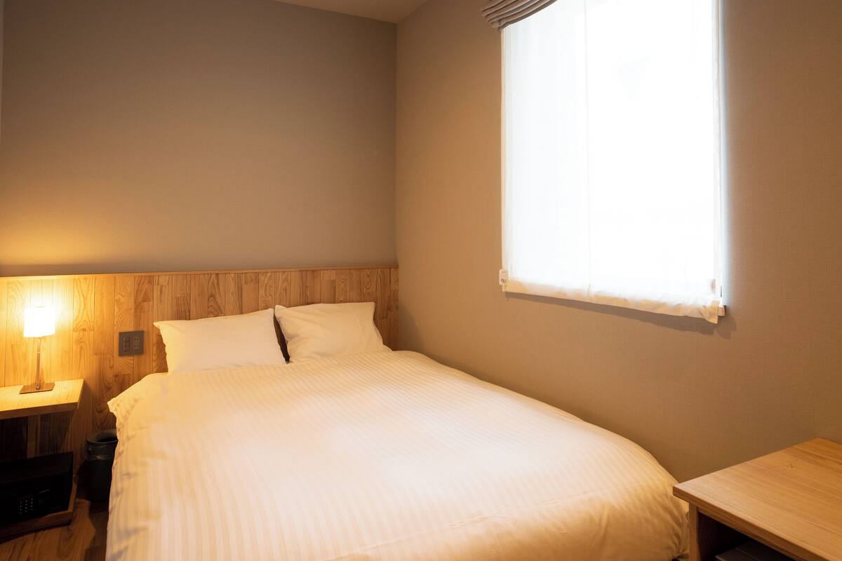 A hotel room with a bed, a nightstand, a lamp, and a window.