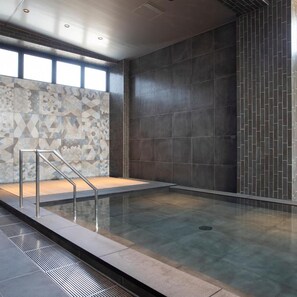 Una piscina interior moderna con un muro de azulejos geométricos y un cerramiento de vidrio transparente.