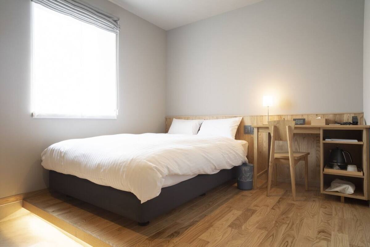 A bedroom with a bed, a desk, a chair, and a window.