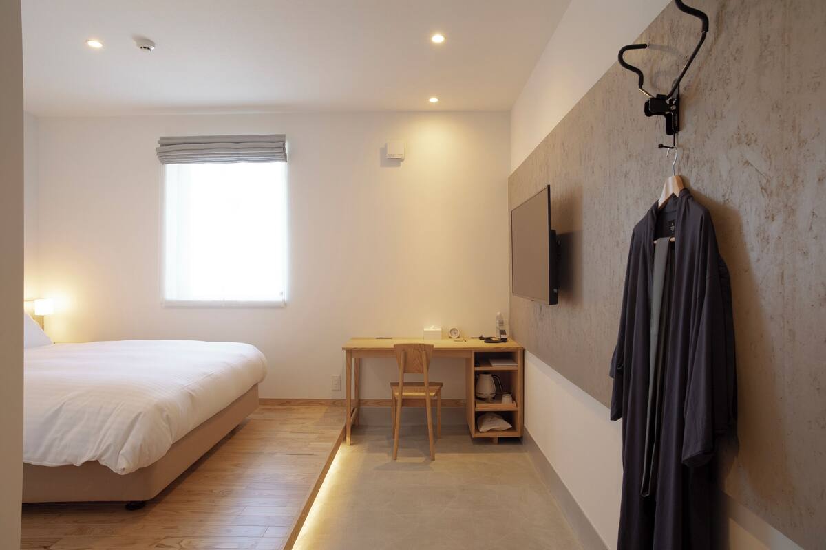 A bedroom with a bed, desk, chair, and a TV mounted on the wall.