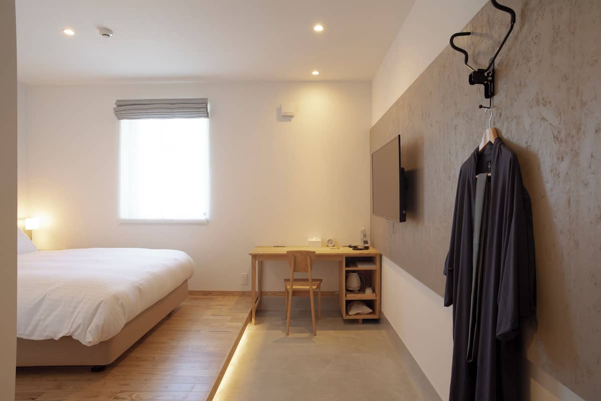 A bedroom with a bed, desk, chair, and a TV mounted on the wall.