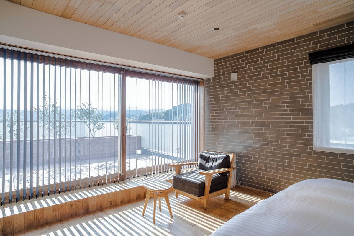 A modern room with a large sliding glass door, a wooden ceiling, a brick wall, and a bed.