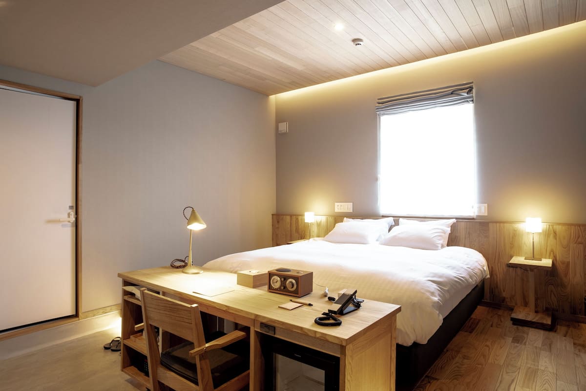 A bedroom with a bed, bedside tables, a desk with a chair, a lamp, and a radio.
