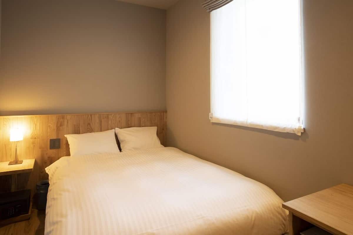 A single bed with a wooden headboard, a bedside table with a lamp, and a window with curtains.