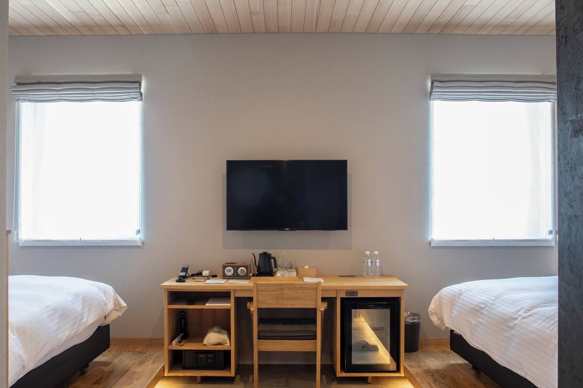 A bedroom with a bed, a desk with a TV, and a window.