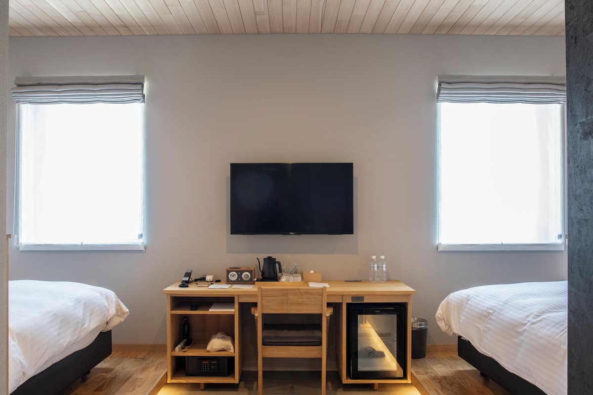 A bedroom with a bed, a desk with a TV, and a window.