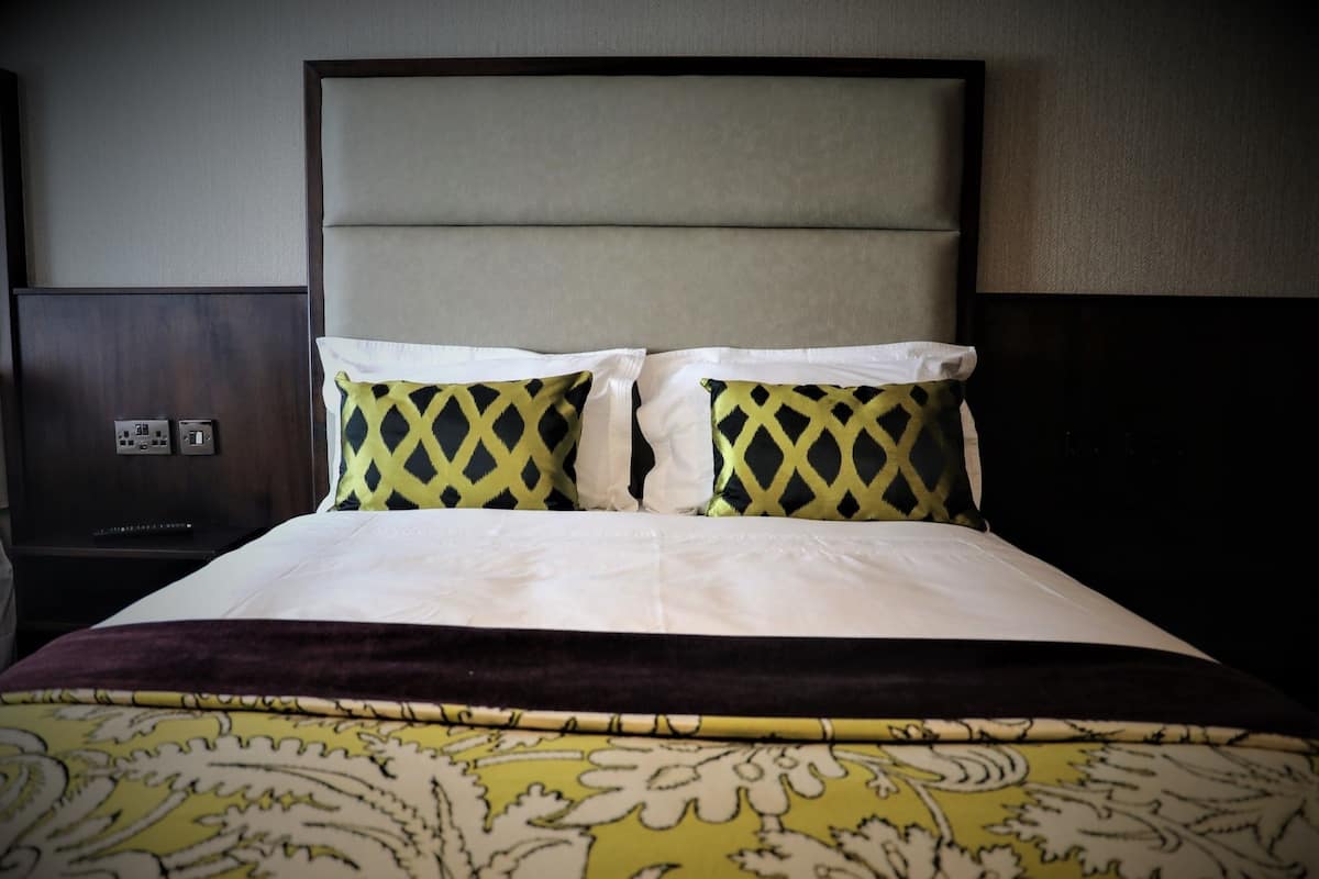 A hotel room with a bed, a headboard, and a nightstand with a lamp.