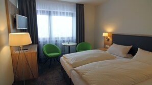 Een hotelkamer met twee bedden, een bureau met lamp, een televisie, twee stoelen en een kleine tafel.