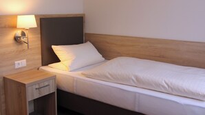 Een hotelkamer met een enkel bed, een nachtkastje, een lamp en een groene stoel.