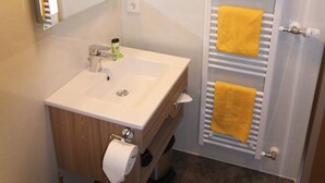 Een badkamer met een wit wastafelmeubel, spiegel en handdoekrek met gele handdoeken.