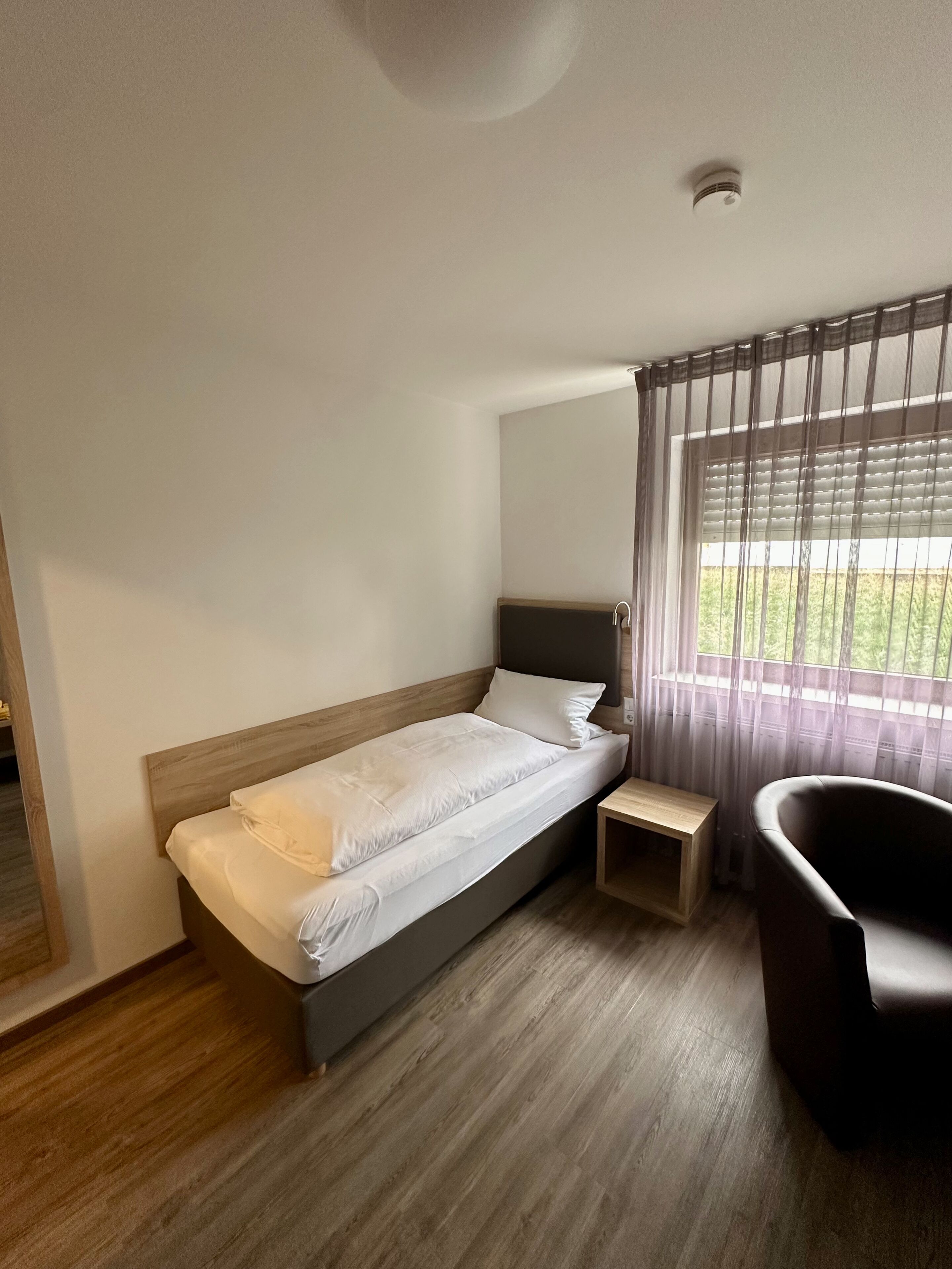 A bedroom with a bed, a bedside table, a chair, and a window with curtains.