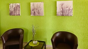 Een kamer met groene wanden, twee bruine fauteuils, een tafeltje met een vaas, en drie plafondlampen.