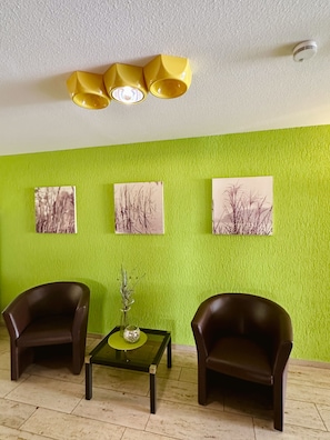 A room with green walls, two brown armchairs, a small table with a vase, and three ceiling lights.