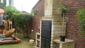 A stone fireplace with a black door, surrounded by a brick wall and a small garden area with a swing chair and potted plants. - Lapeng Home Away from Home (Maseru)