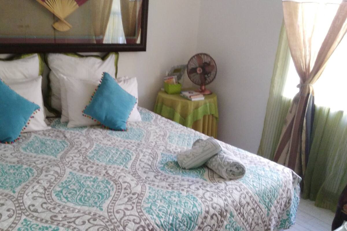 A bed with patterned bedding, two pillows, and a pair of slippers on it.