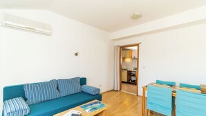 A living room with a teal sofa, a wooden coffee table, and a dining area with blue chairs. - Apartmani Princ Hrvoje (Dubrovnik)