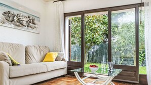 A living room with a sofa, a glass coffee table, and a large window with a view of greenery. - Puig Dels Daus by Interhome (Calonge)
