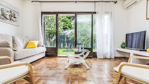 A living room with a sofa, a glass-top table, and chairs. There is a TV on a stand and a painting on the wall. - Puig Dels Daus by Interhome (Calonge)