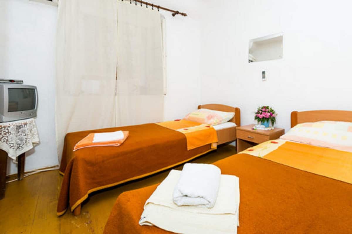 A room with two single beds, a small bedside table with a lamp, a television on a stand, and a curtain.