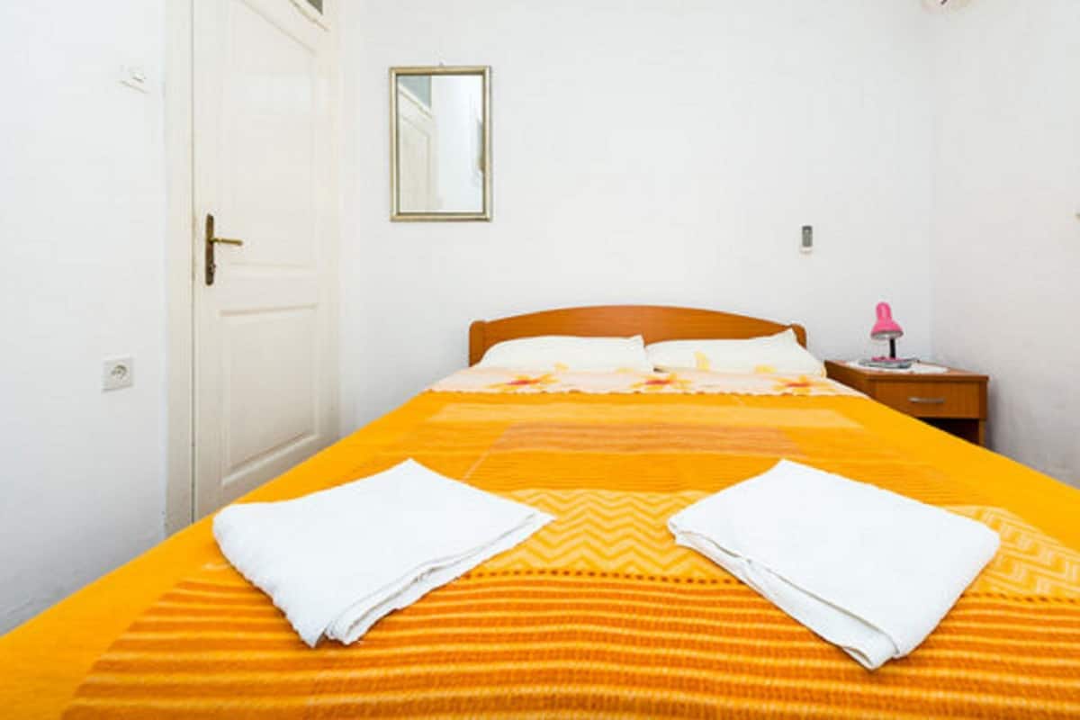 A neatly made bed with a striped orange bedspread and two folded white towels.