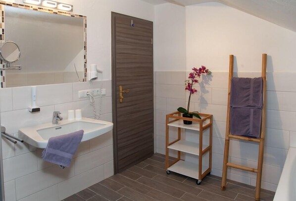 A bathroom with a sink, mirror, door, and a shelf with a plant. - Pension Bavaria (Mittenwald)