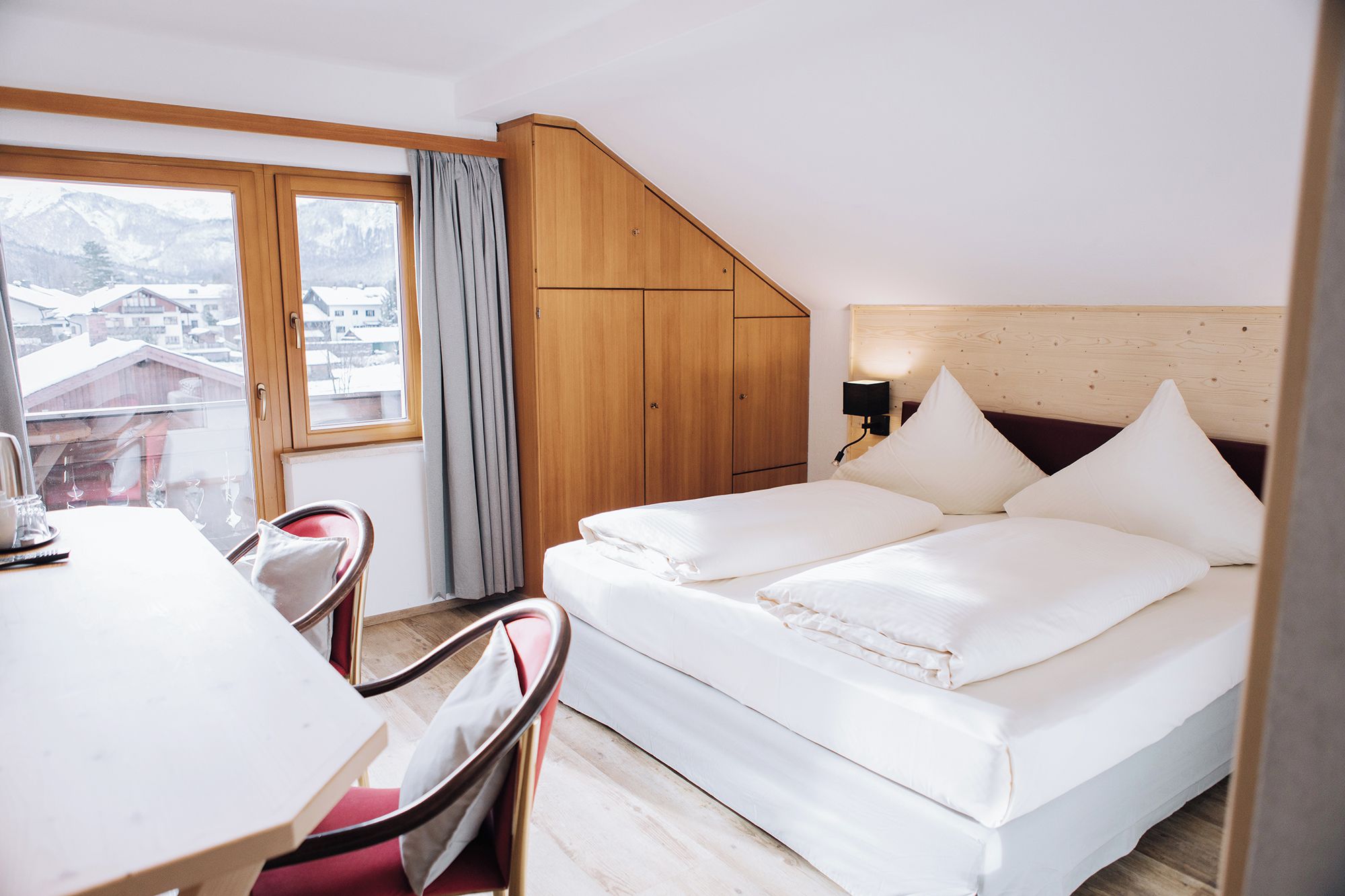 A bedroom with a bed, a desk, a chair, and a window with curtains.