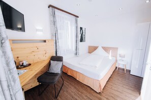 Hotellihuone, jossa on sänky, työpöytä, tuoli, televisio ja yöpöytä.
