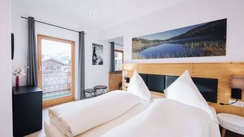 Ein Hotelzimmer mit Bett, Nachttisch, Stuhl, einem Fenster mit Vorhängen, einem Bild und Blick auf ein Gebäude.