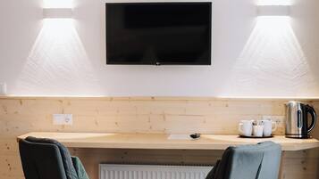 Ein modernes Zimmer mit einem wandmontierten Flachbildfernseher, zwei Stühlen mit Metallbeinen, einer Holzauslage mit einem Wasserkocher und einem Heizkörper darunter.