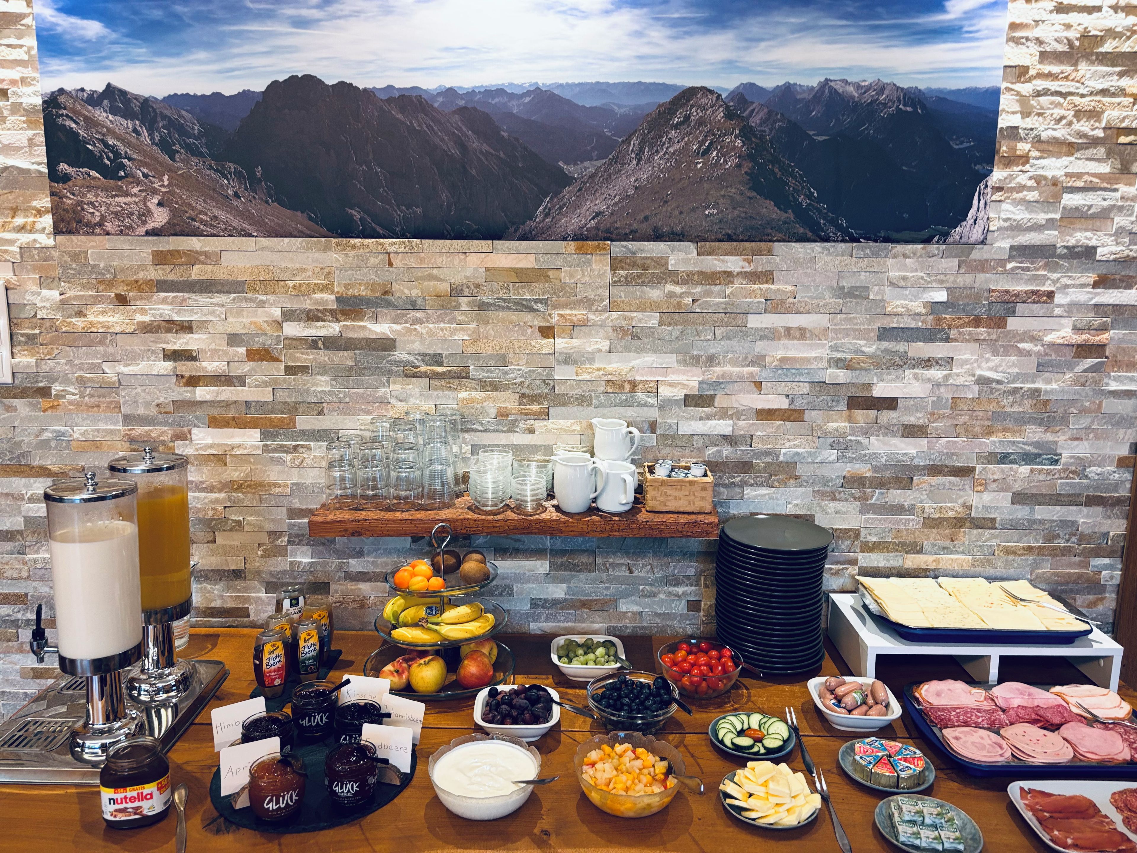 A buffet setup with a mountain view backdrop, featuring a variety of food items and beverages.