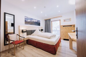 Ein Hotelzimmer mit Bett, Schreibtisch, Stuhl, Spiegel, Fenster mit Vorhängen und einem Wandbild.