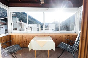 Una habitación con una mesa y dos sillas, un ventanal con vistas a una montaña y edificios, y paneles de madera.