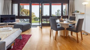 A modern living room with a sofa, a TV, a dining table with chairs, and large windows with curtains. - Krokus Apt.T by Interhome (Wengen)