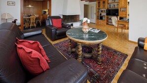 A living room with a sofa, a coffee table, a fireplace, a bookshelf, and a dining area. - Chalet Shangri La by Interhome (Grindelwald)