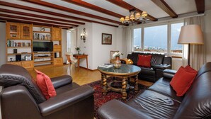 A living room with leather sofas, a coffee table, a bookshelf, and a view of a cityscape through large windows. - Chalet Shangri La by Interhome (Grindelwald)