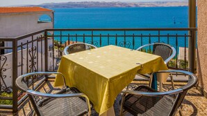Balcón con mesa y sillas con vista a una masa de agua y colinas distantes.