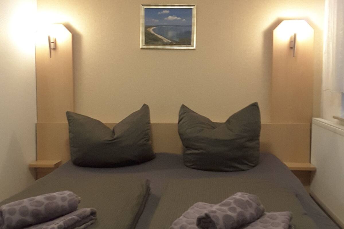 Habitación doble con dos camas, cada una con una almohada y una colcha, un cuadro en la pared y dos lámparas de pared.