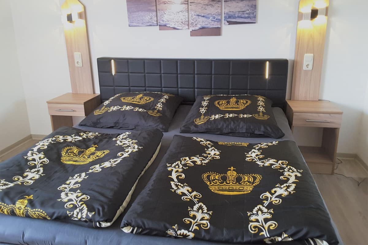 Una cama con cabecera oscura, dos mesitas de noche y un aplique de pared.