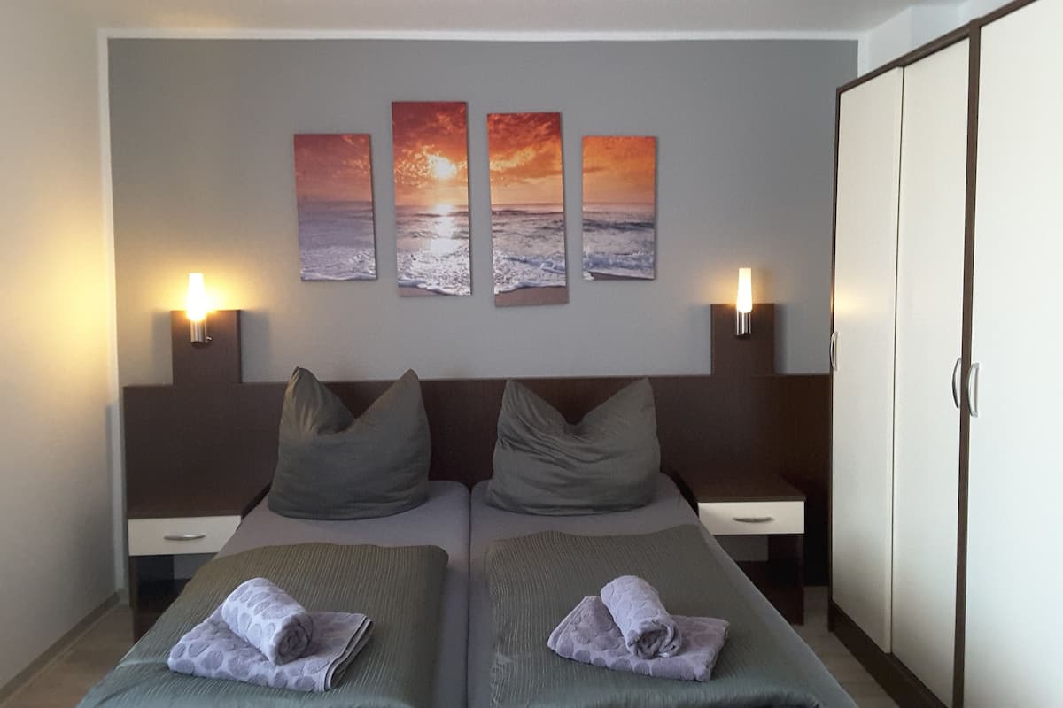 Una habitación de hotel con una cama, dos mesitas de noche, un armario y tres cuadros del atardecer en la pared.