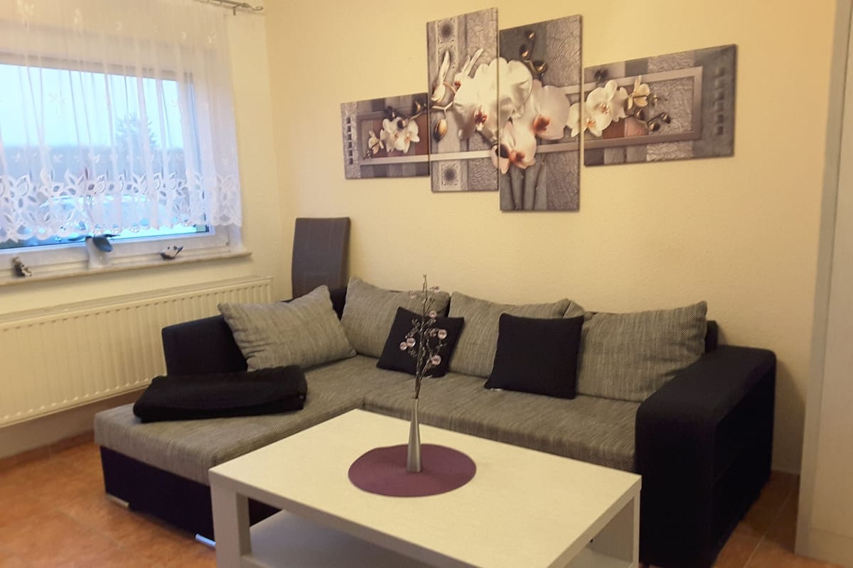 Una sala de estar con un sofá gris, una mesita de centro blanca y una obra de arte en la pared con flores blancas.