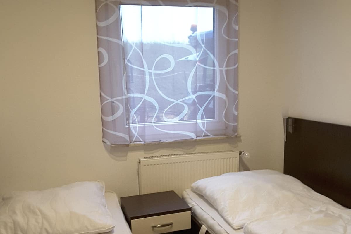 Una habitación de hotel pequeña y sencilla con dos camas, una mesita de noche y una ventana con cortinas.