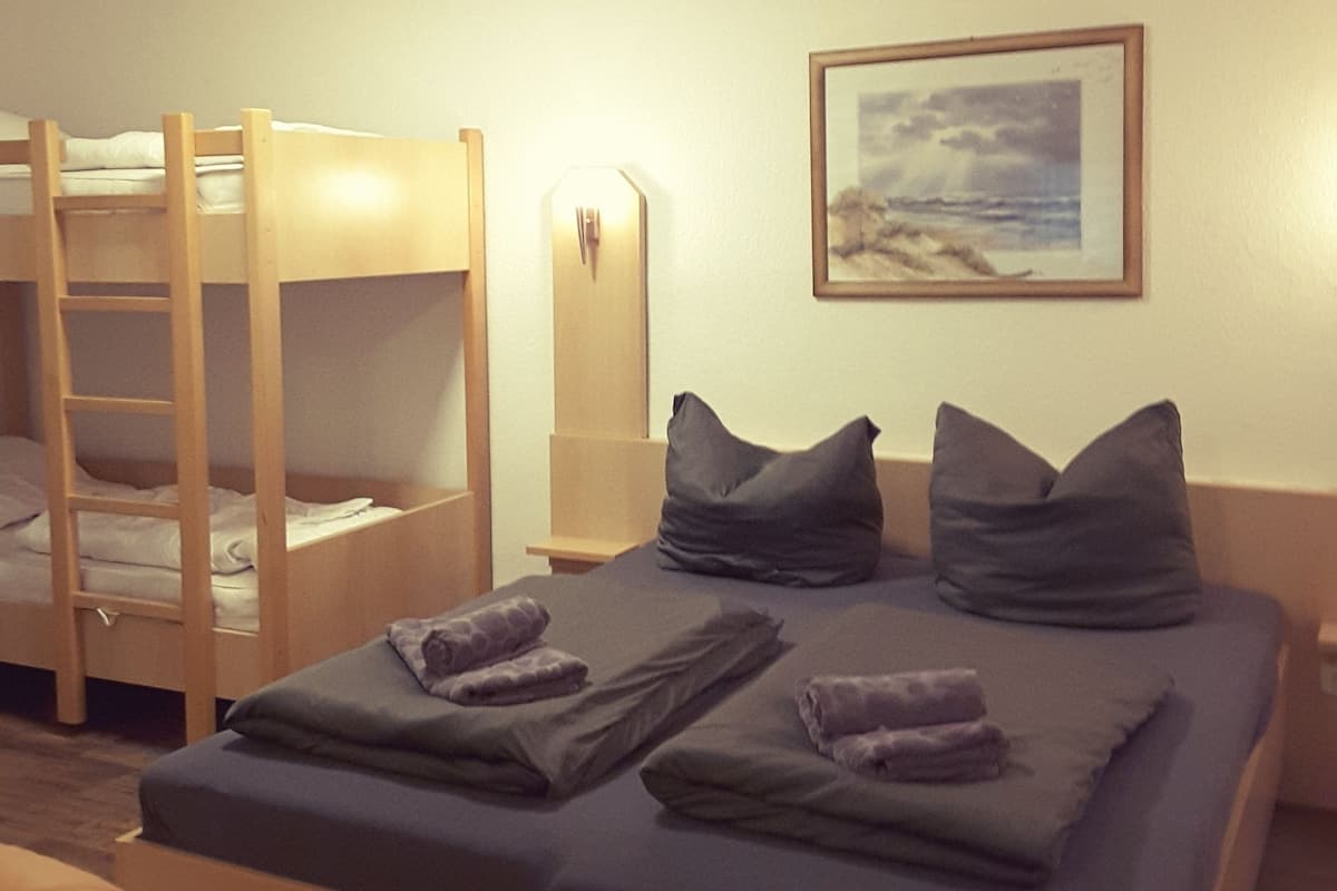 Una habitación con literas, una cama con almohadas, una mesita de noche y un cuadro en la pared.