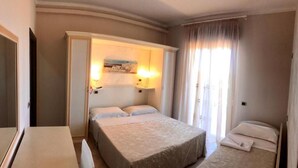 A hotel room with a bed, a bedside table, a lamp, and a window with curtains.