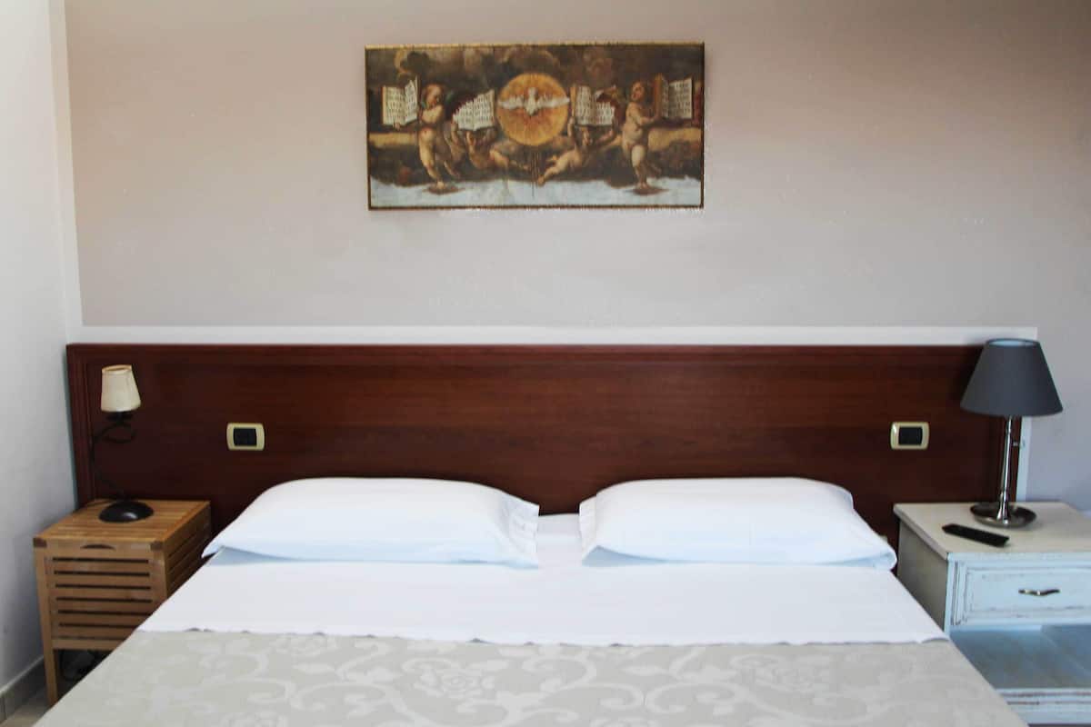 Ein Hotelzimmer mit hölzernem Kopfteil, zwei Nachttischen mit Lampen, einem Bett mit weißer Bettwäsche und einem Gemälde an der Wand.