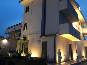 Un bâtiment moderne à plusieurs étages, doté d’un éclairage extérieur lumineux, d’une statue à l’avant et surplombant un ciel dégagé.